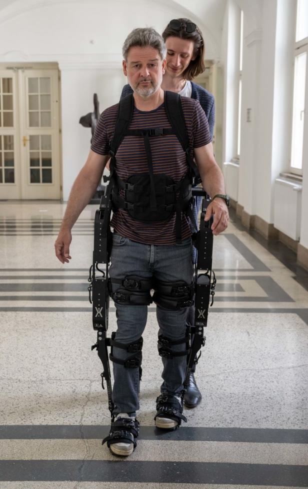 Ein Mann geht mit einem Exoskelett, während eine andere Person ihn unterstützt.