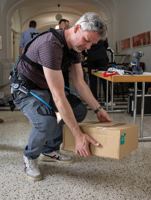 Ein Mann mit einem Exoskelett hebt eine Kiste an.