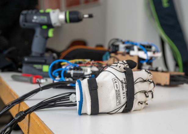 Ein Arbeitshandschuh mit Sensoren und Kabeln liegt auf einem Tisch, im Hintergrund Werkzeuge.