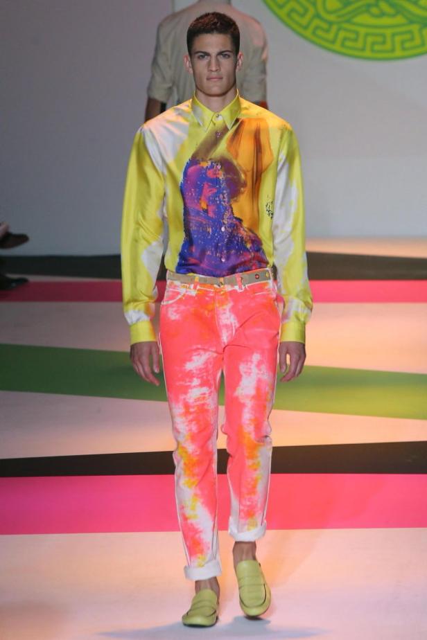 Ein Mann in einem gelb-weißem Hemd mit abstraktem Aufdruck und einer pinkfarbenen Hose auf einem Laufsteg.