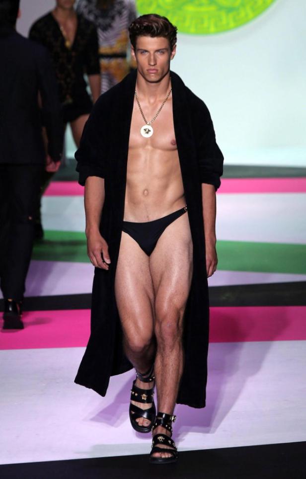 Ein Mann mit schwarzem Bademantel und Sandalen auf einem Laufsteg.