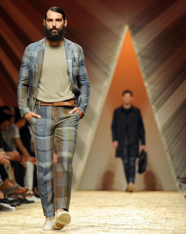 Ein bärtiger Mann in einem karierten Anzug läuft auf einem Laufsteg.