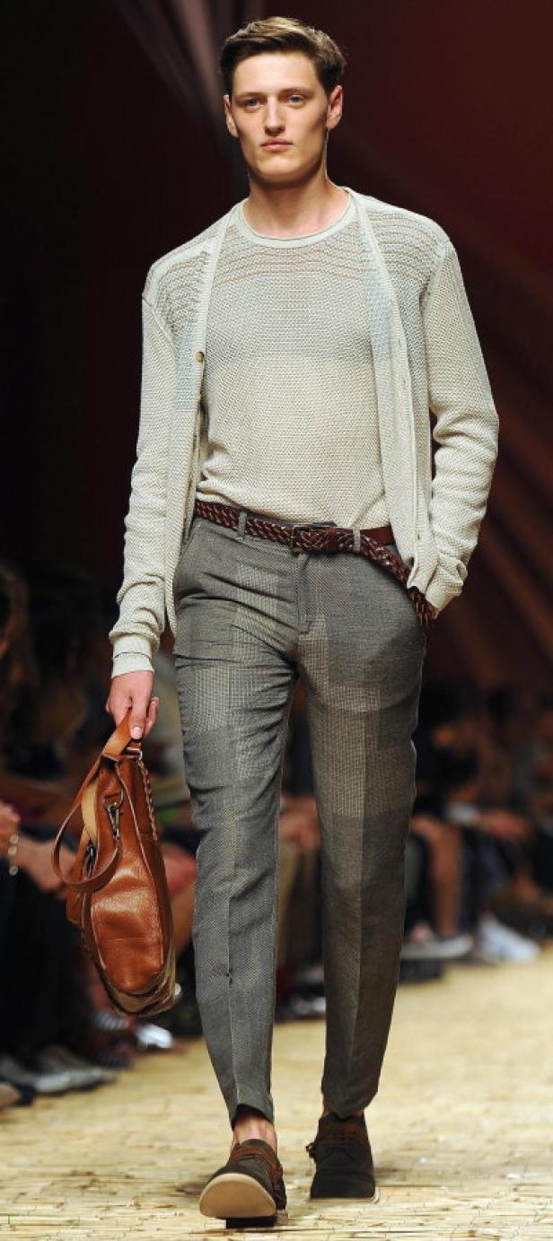 Ein Mann in Strickjacke, Hose und Ledertasche auf einem Laufsteg.