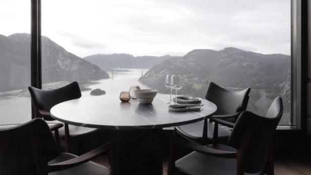 Ein Esstisch mit Gedeck vor einer malerischen Berglandschaft.