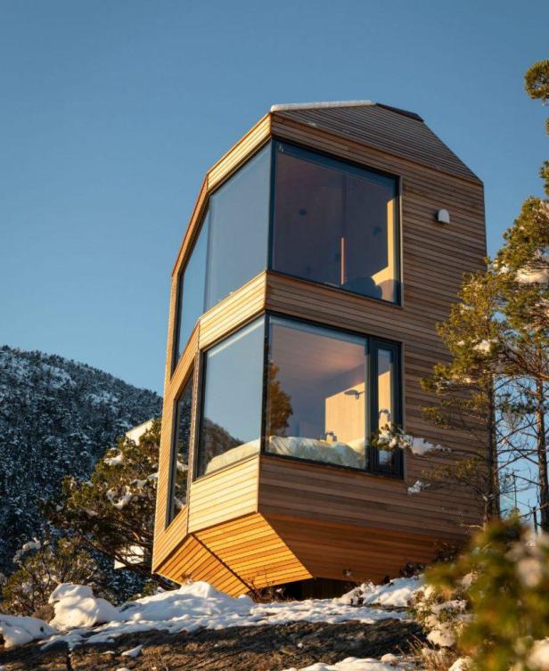Die Bolder Star Lodge, ein modernes Holzhaus mit großen Fenstern, steht auf einem schneebedeckten Felsen.