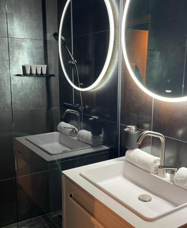 Ein modernes Badezimmer mit Waschbecken, Spiegeln und dunklen Fliesen.