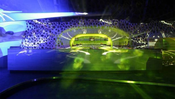 Eine Bar mit Flaschenregalen ist in einem futuristischen Club mit blauen und grünen Lichtern zu sehen.