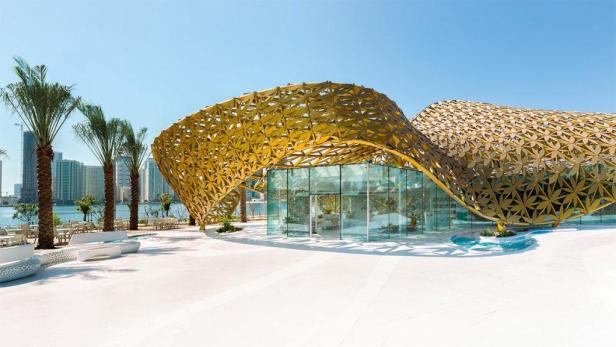 Ein Gebäude mit modernem, orientalischem Design und einer goldenen Fassade am Wasser.