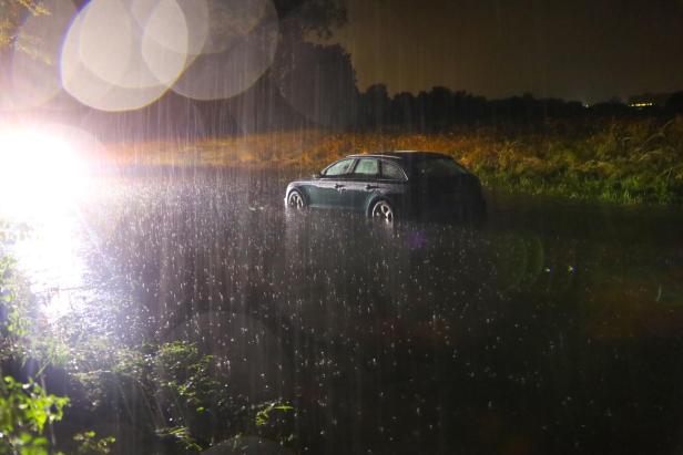 Ein dunkler Kombi steht nachts im Regen auf einem Feld.