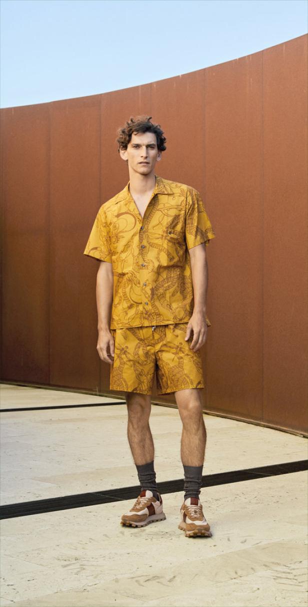 Ein Mann posiert in einem gelben Hemd und Shorts mit Schlangenmuster vor einer Wand.