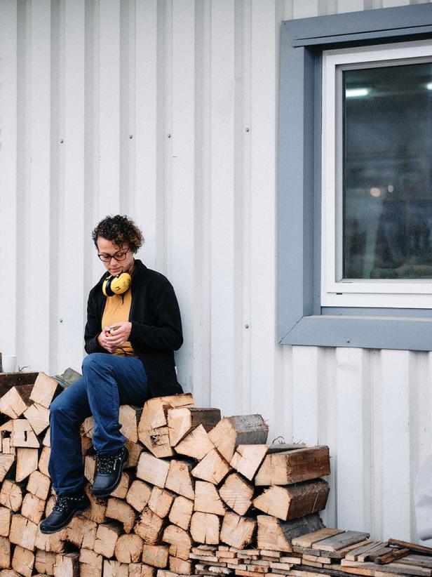 Katja Kammerer und Philipp Horak sitzen auf einem Holzstapel vor einer Wand.