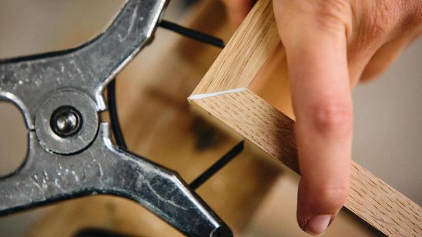 Eine Person leimt und fixiert einen hölzernen Bilderrahmen mit einer Klammer.