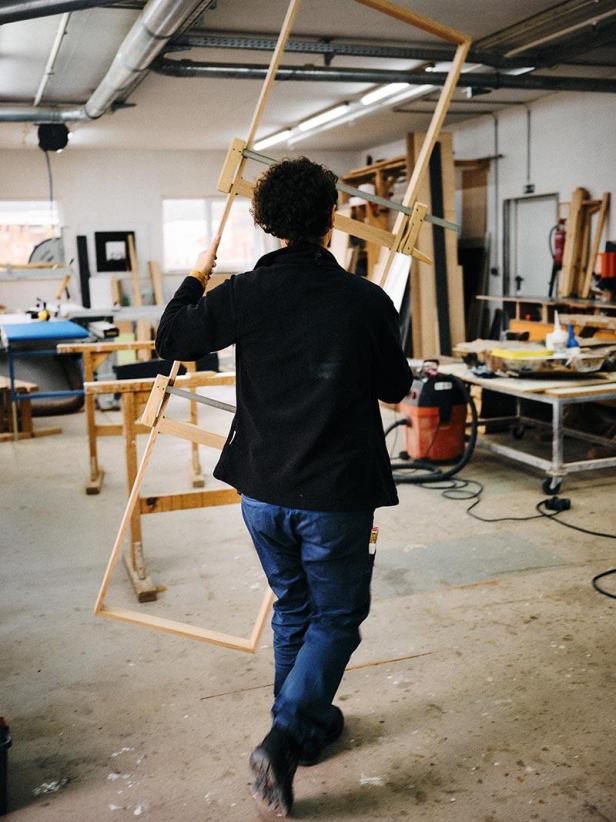 Eine Person trägt einen Holzrahmen durch eine Werkstatt.