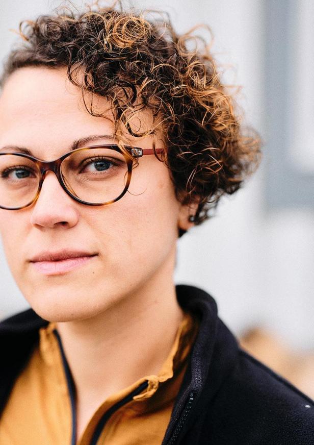 Porträt einer Frau mit lockigem Haar und Brille.