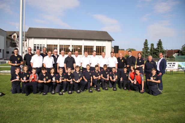 Eine Gruppe von Feuerwehrleuten und Jugendlichen posiert auf einer Wiese für ein Foto.