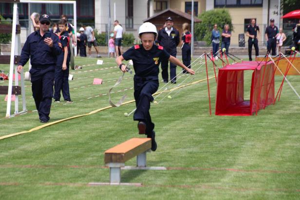 Ein junger Feuerwehrmann springt über eine Bank bei einem Wettbewerb.