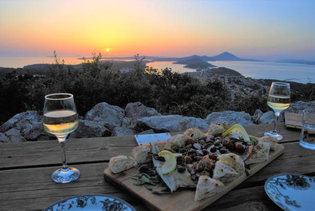 Ein Abendessen mit Fisch und Wein auf einem Tisch mit Blick auf das Meer bei Sonnenuntergang.