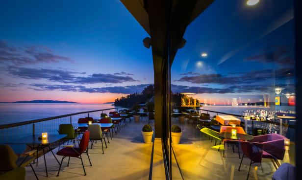 Ein Restaurant mit Tischen und Stühlen bietet einen Blick auf das Meer bei Sonnenuntergang.