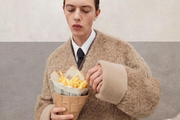Ein Mann im Mantel isst Pommes Frites aus einer Papiertüte.