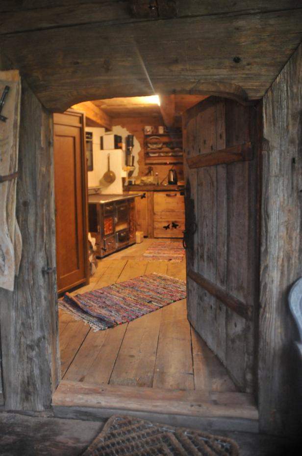 Blick durch eine offene Holztür in eine rustikale Küche.