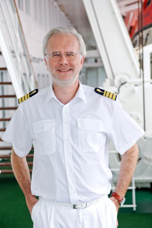 Ein lächelnder Kapitän in Uniform steht auf einem Schiff.
