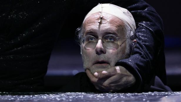 Ein Mann mit Brille und Kappe wird von einer Hand am Hals gehalten.