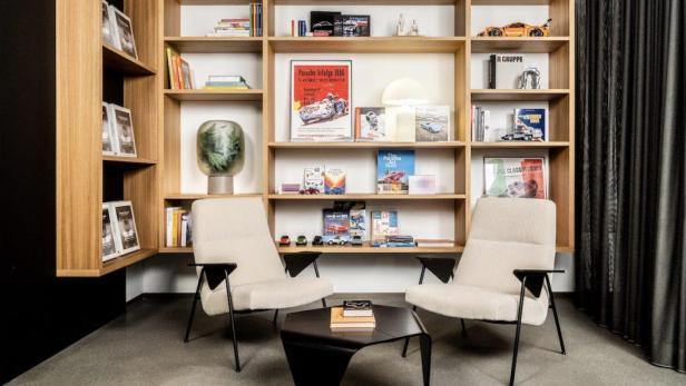 Zwei Sessel und ein Tisch vor einem Regal mit Porsche-Literatur und -Modellen.
