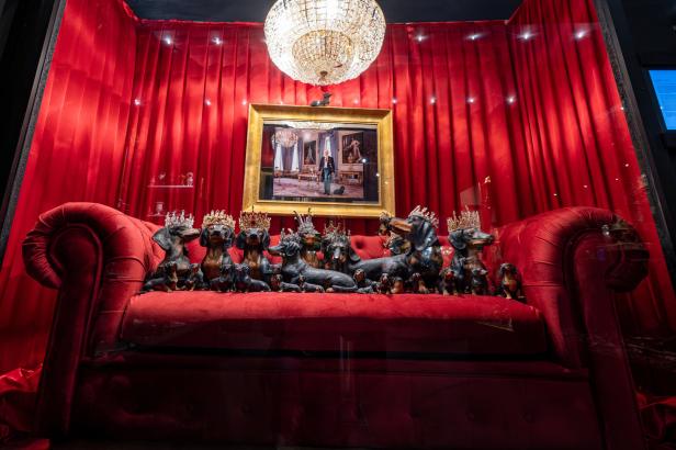 Eine Gruppe Dackel-Statuen mit Kronen sitzt auf einem roten Sofa vor einem roten Vorhang.
