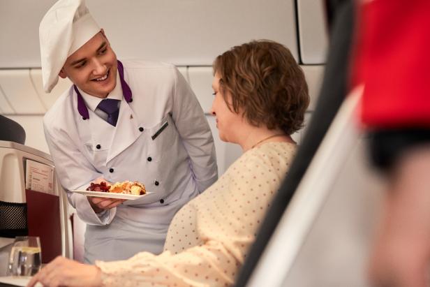 Ein Koch serviert einer Frau ein Dessert in einem Flugzeug.