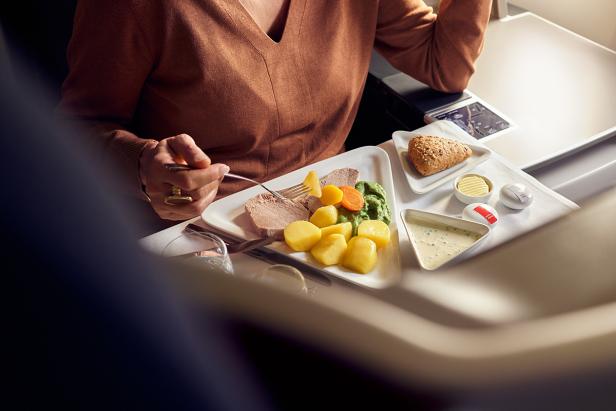 Eine Person isst ein Gericht mit Fleisch, Kartoffeln und Gemüse an Bord eines Flugzeugs.