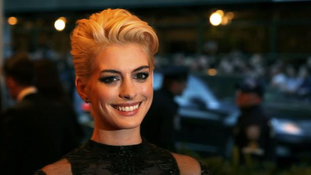 Anne Hathaway lächelt mit blonden Haaren vor einer Menschenmenge.