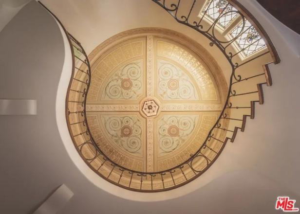 Blick von unten auf ein kunstvoll bemaltes Deckengemälde und ein geschwungenes Treppengeländer.
