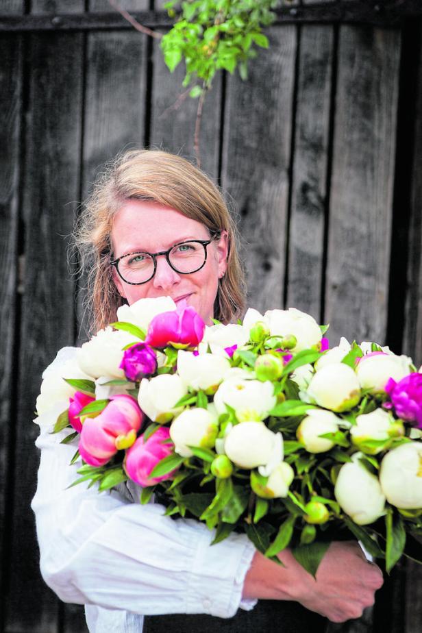 Eine Frau mit Brille hält einen üppigen Strauß weißer und pinkfarbener Pfingstrosen.