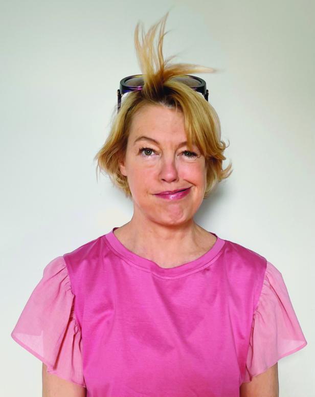 Eine Frau mit blonden Haaren und Sonnenbrille auf dem Kopf zwinkert in die Kamera.