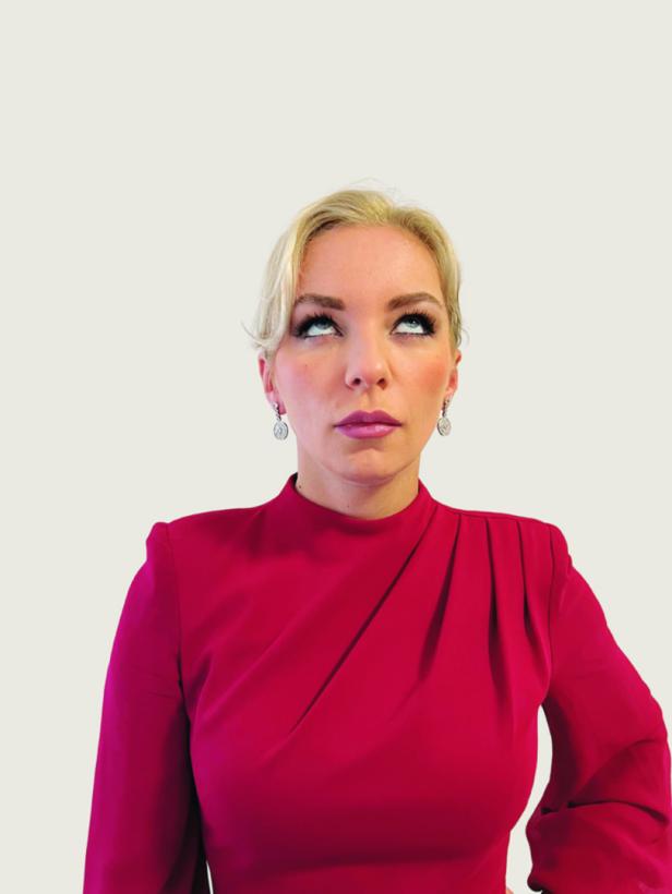 Eine Frau mit blonden Haaren und rotem Kleid blickt nach oben.
