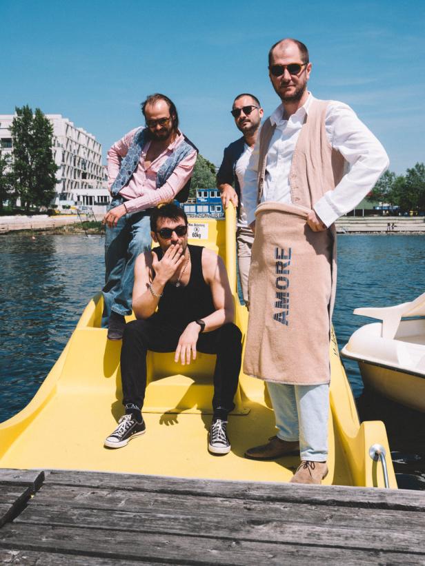 Vier Männer posieren auf einem gelben Tretboot auf einem See.