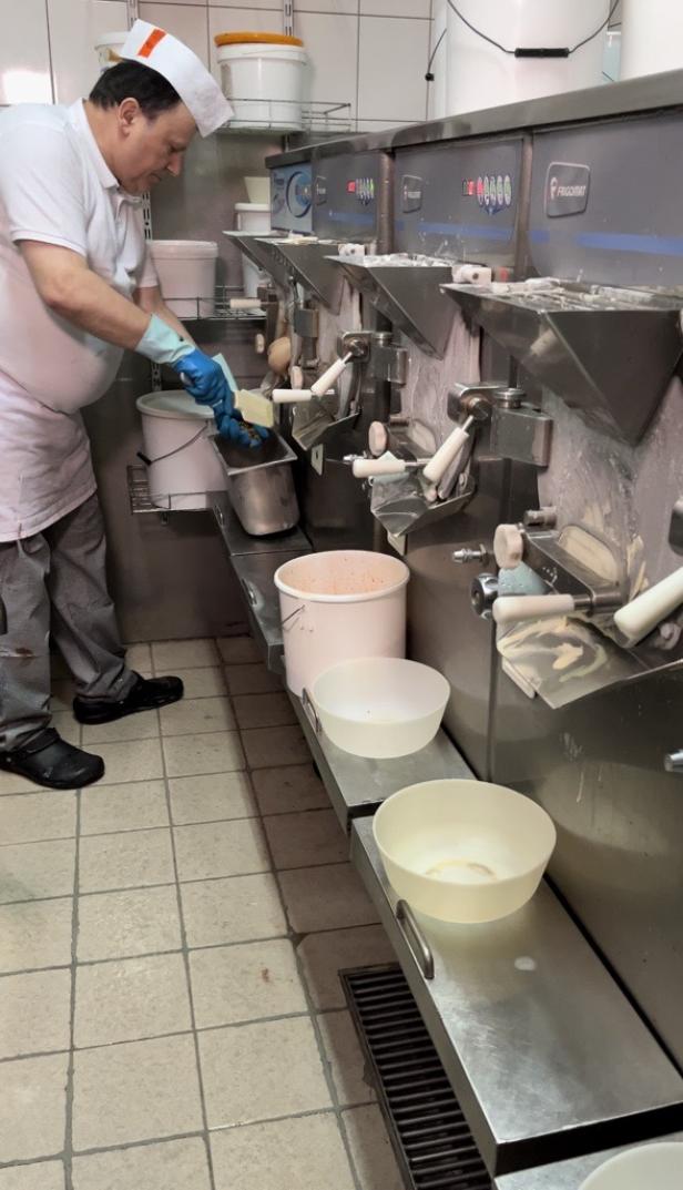 Ein Mann mit Kochmütze und Handschuhen arbeitet an einer Eismaschine.