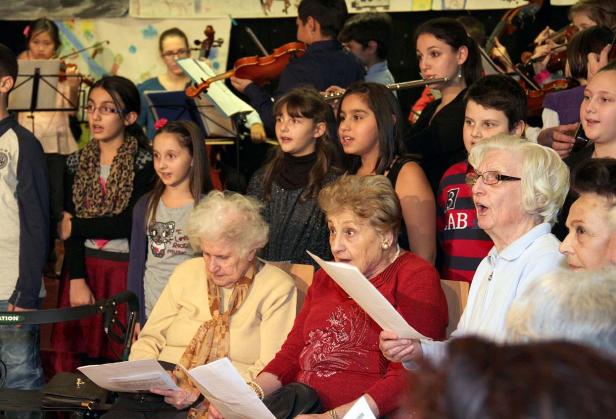 Ein Chor aus Kindern und älteren Menschen singt gemeinsam mit Orchesterbegleitung.