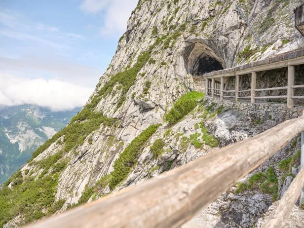 Ein gesicherter Weg führt zu einer Höhle in einem steilen Bergmassiv.