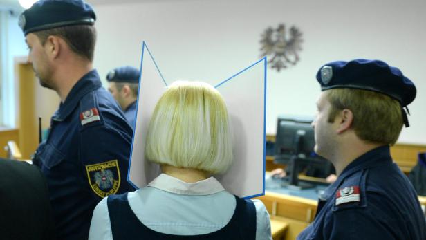 Eine Frau mit blonden Haaren in einem Gerichtssaal, bewacht von Justizbeamten.