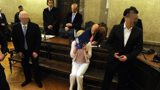 Eine Frau versteckt ihr Gesicht hinter einer blauen Akte in einem Gerichtssaal.