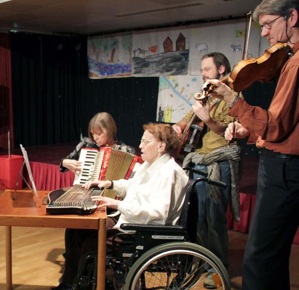 Eine Musikgruppe spielt mit Zither, Akkordeon, Gitarre und Geige auf einer Bühne.