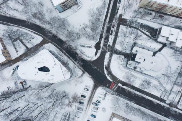 Eine verschneite Wohngegend mit Straßen, Häusern und geparkten Autos aus der Vogelperspektive.
