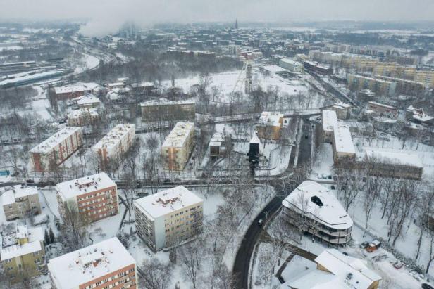 Eine verschneite Stadtlandschaft mit Wohngebäuden und einem Förderturm im Hintergrund.