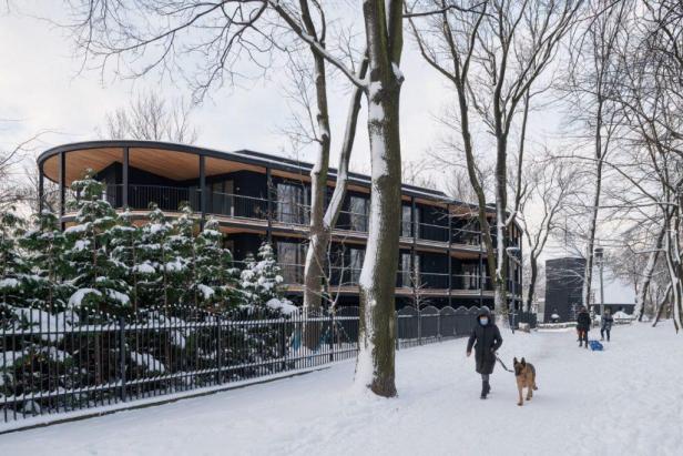 Eine Frau geht mit ihrem Hund an einem verschneiten Tag an einem modernen Gebäude vorbei.