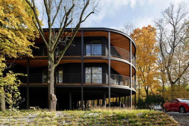 Ein modernes, dreistöckiges Gebäude mit runden Balkonen, umgeben von Bäumen im Herbst.