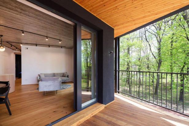 Blick von einem modernen Balkon auf einen hellen Wohnraum und grüne Bäume.