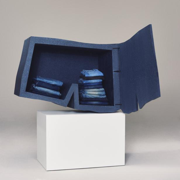 Ein Regal in Form einer Jeans, gefüllt mit Jeansstapeln, steht auf einem weißen Sockel.