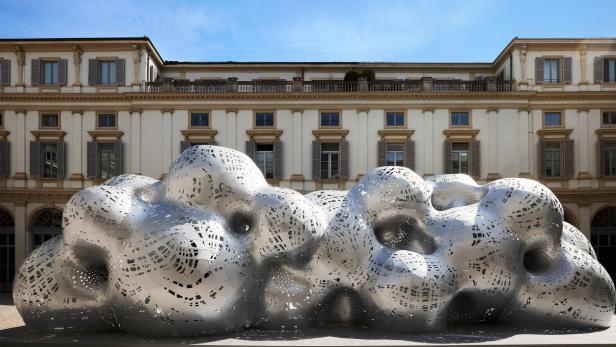 Eine skulpturale, wolkenartige Struktur aus Metall steht vor einem Gebäude.