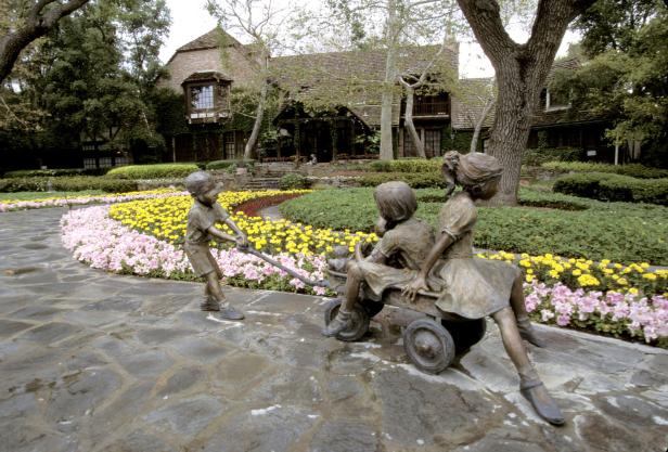 Eine Bronzeskulptur von Kindern mit einem Wagen in einem Garten.
